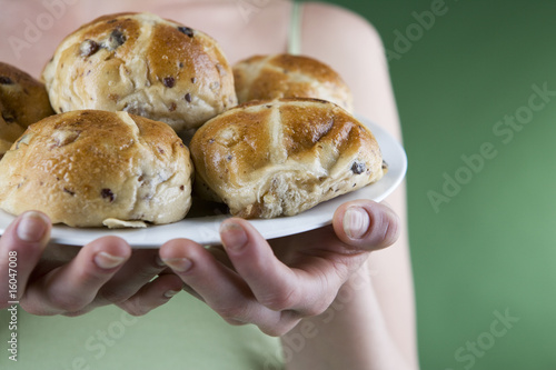 Photo: A young woman holding a plate of hot cross buns, close-up A young woman holding a plate of hot cross buns, close-up