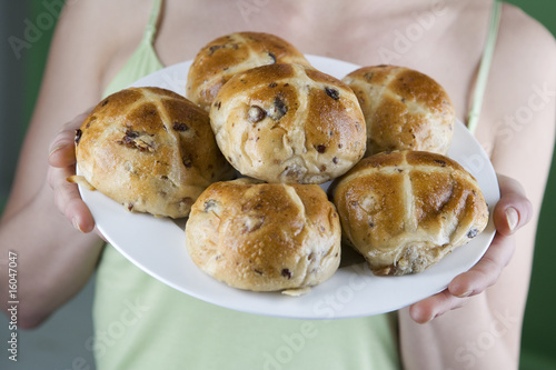 Photo: A young woman holding a plate of hot cross buns, close-up A young woman holding a plate of hot cross buns, close-up