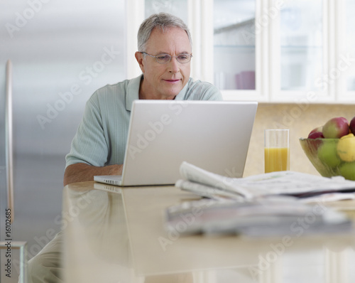 Photo: Man in kitchen using laptop Man in kitchen using laptop