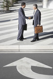 Photo: Two businessmen outdoors shaking hands by street with arrow pointing towards them Two businessmen outdoors shaking hands by street with arrow pointing towards them