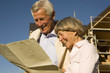 Senior couple holding plan in front of partially built house