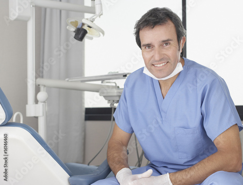 Photo: Dentist sitting in examination room smiling Dentist sitting in examination room smiling