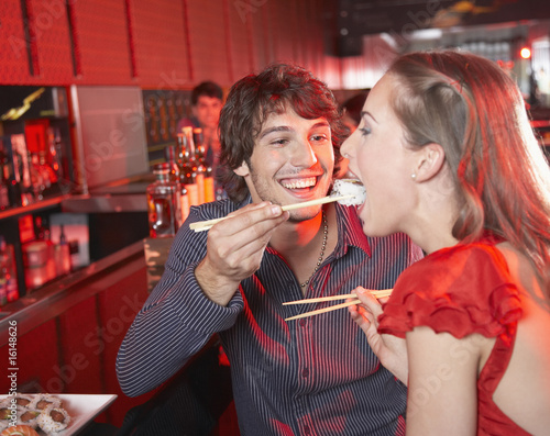 Photo: Man feeding woman sushi in nightclub and smiling Man feeding woman sushi in nightclub and smiling