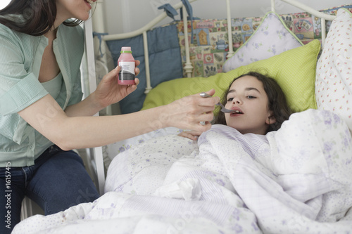 Photo: Woman helping young girl take medicine in bedroom Woman helping young girl take medicine in bedroom