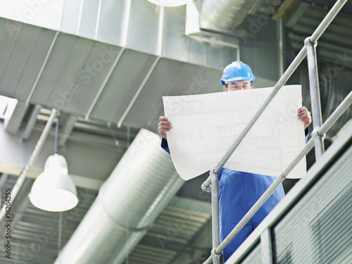 Photo: Businessman in hard-hat looking at blueprints Businessman in hard-hat looking at blueprints