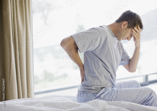 Photo: Man sitting on bed with backache and headache Man sitting on bed with backache and headache