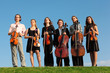 Six violinists stand on  grass against sky