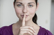junge schöne frau legt geheimnisvoll finger auf lippen
