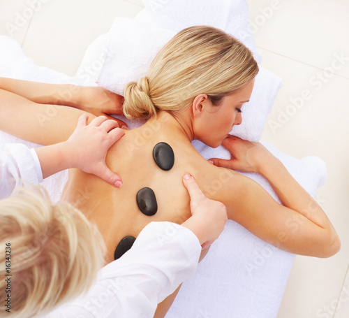 Photo: Hot stone therapy - Young woman getting a back massage by a mass Hot stone therapy - Young woman getting a back massage by a mass