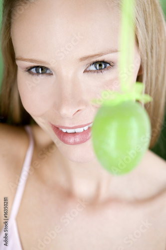 Photo: A young blonde woman holding a green Easter egg, close-up A young blonde woman holding a green Easter egg, close-up