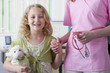 Smiling girl with stuffed animal holding nurseճ hand in examination room