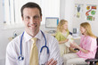Doctor smiling in office with woman and girl in background