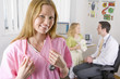 Nurse smiling in office with doctor and girl in background