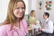 Nurse in office smiling with doctor and girl in background