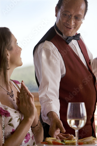 Photo: Waiter serving food to woman at patio table Waiter serving food to woman at patio table
