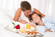 Young smiling couple having luxury breakfast in hotel room