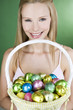 A young woman holding a basket full of Easter eggs, smiling
