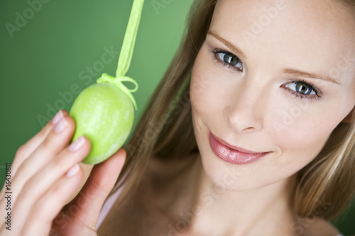 Photo: A young blonde woman holding a green Easter egg, close-up A young blonde woman holding a green Easter egg, close-up