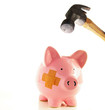 Piggy bank with bandage about to be smahed by a hammer Piggy bank with bandage about to be smahed by a hammer