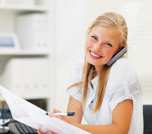 Foto: Portrait of a woman speaking on the phone, reading a document Portrait of a woman speaking on the phone, reading a document
