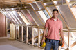 Smiling electrician standing in attic under construction