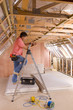 Electrician using meter on ladder in attic under construction
