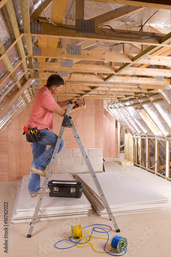 Photo: Electrician using meter on ladder in attic under construction Electrician using meter on ladder in attic under construction