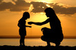 Silhouette of the women to pour sand in hand child on sundown Silhouette of the women to pour sand in hand child on sundown