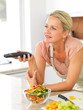 Middle aged woman with the TV remote while preparing dinner in t Middle aged woman with the TV remote while preparing dinner in t