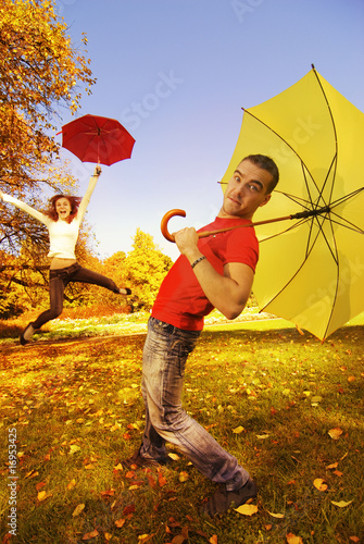 Photo: Funny couple with umbrellas on autumn background (focus on a guy Funny couple with umbrellas on autumn background (focus on a guy