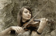 Beautiful female violinist playing violin on the grunge backgrou