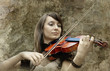 Beautiful female violinist playing violin on the grunge backgrou