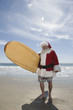 Father Christmas stands with a surfboard at the beach