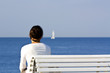 Frau auf Bank mit Segelboot am Horizont Frau auf Bank mit Segelboot am Horizont