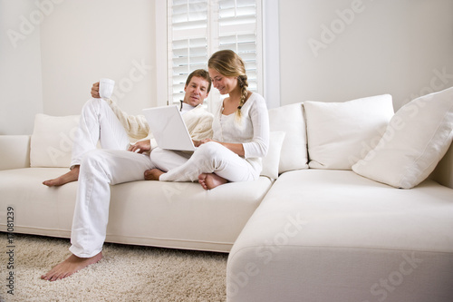Photo: Father and teen daughter on white living room sofa using laptop Father and teen daughter on white living room sofa using laptop