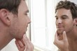 unshaven man looking in bathroom mirror