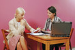 two young women discuss on pink