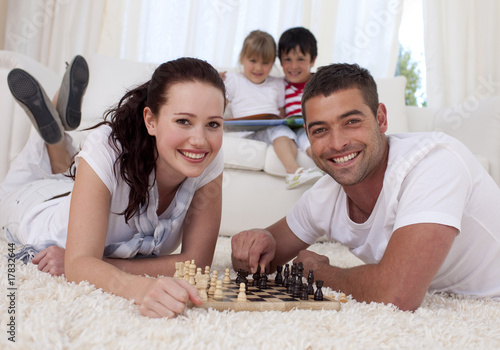Photo: Happy couple playing chess on floor in living-room Happy couple playing chess on floor in living-room