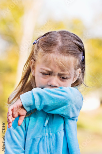 Photo: Young child coughing or sneezing into her elbow. Young child coughing or sneezing into her elbow.