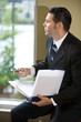 Businessman looking out office window holding binder