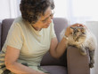 Senior Hispanic woman petting cat on sofa