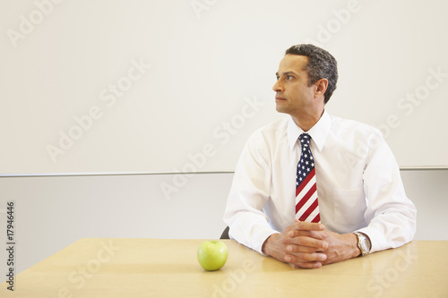 Photo: Hispanic male teacher with American flag tie and apple on desk Hispanic male teacher with American flag tie and apple on desk