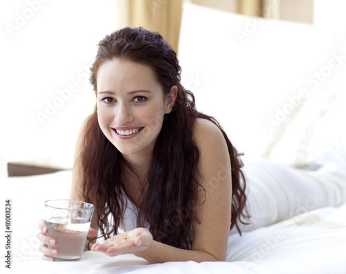 Photo: Woman in bed taking pills with water Woman in bed taking pills with water