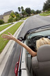 Young Woman Driving Convertible Car With Hand In The Air