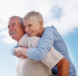 Older man giving woman piggyback ride against cloudy sky