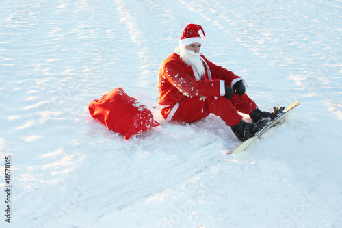 Photo: Weihnachtsmann mit Snowboard sitzt im Schnee Weihnachtsmann mit Snowboard sitzt im Schnee