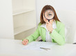 Young woman sits at table with big magnifier in hands Young woman sits at table with big magnifier in hands