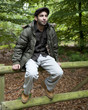 Man sitting on a fence in woodland.