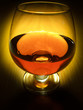 Glass of brandy over wooden background on dark