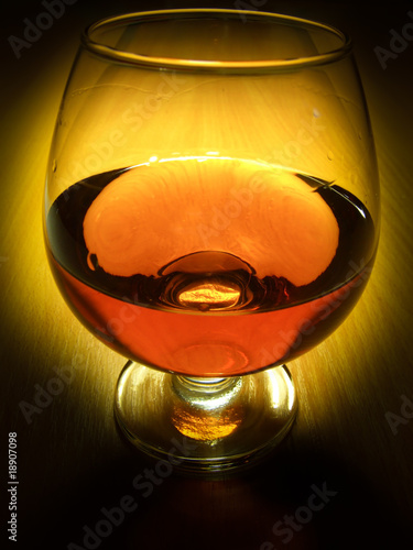 Photo: Glass of brandy over wooden background on dark Glass of brandy over wooden background on dark